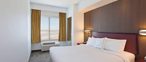 Habitación de hotel con una cama grande, una ventana con cortinas, una lámpara de pared y un cabecero de madera.