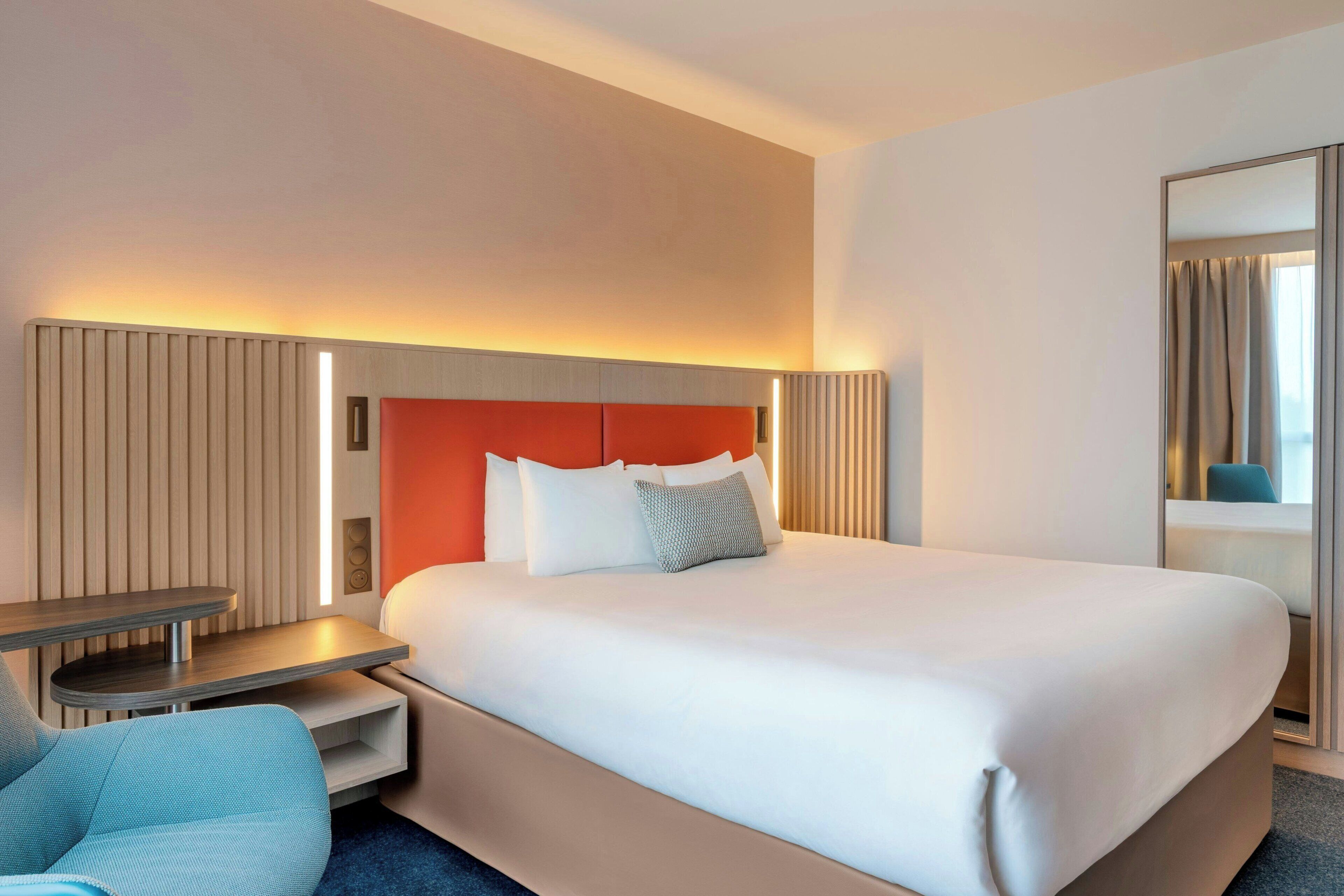 Camera d'albergo con un letto grande, comodini, una sedia e uno specchio.
