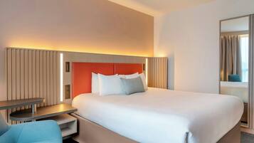 Camera d'albergo con un letto grande, comodini, una sedia e uno specchio.