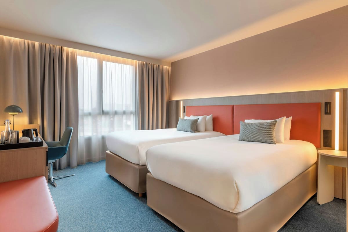 A hotel room with two beds, a desk, a chair, and a small table.