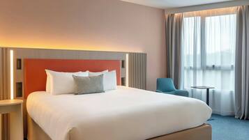 Una habitación de hotel con una cama grande, una mesita de noche, una silla, una pequeña mesa y una ventana con cortinas.