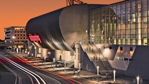 A modern building with a curved facade, large windows, and a staircase leading to an upper level. - Nürburgring Motorsport Hotel (Nuerburg)