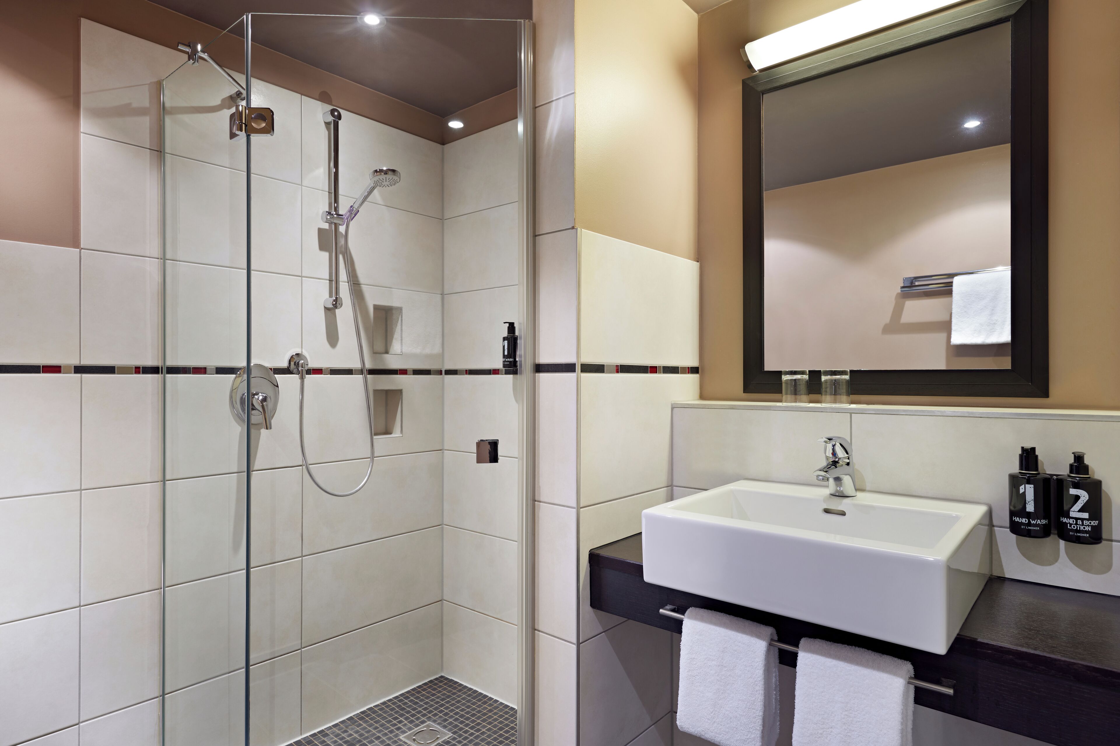 Een moderne badkamer met een douchecabine van glas, een witte wastafel en een grote spiegel.