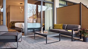 A modern outdoor seating area with a sofa, armchair, and coffee table, featuring a view through large glass doors. - Nürburgring Motorsport Hotel (Nuerburg)