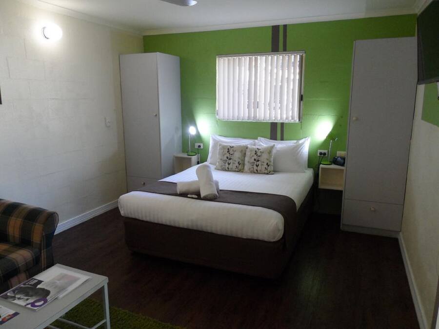 Quarto com cama, guarda-roupa, mesa de cabeceira, abajur e cadeira.