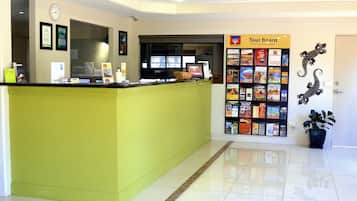 A reception area with a green counter, a clock, framed certificates, a digital display, and a 'Tour Board' sign with brochures.
