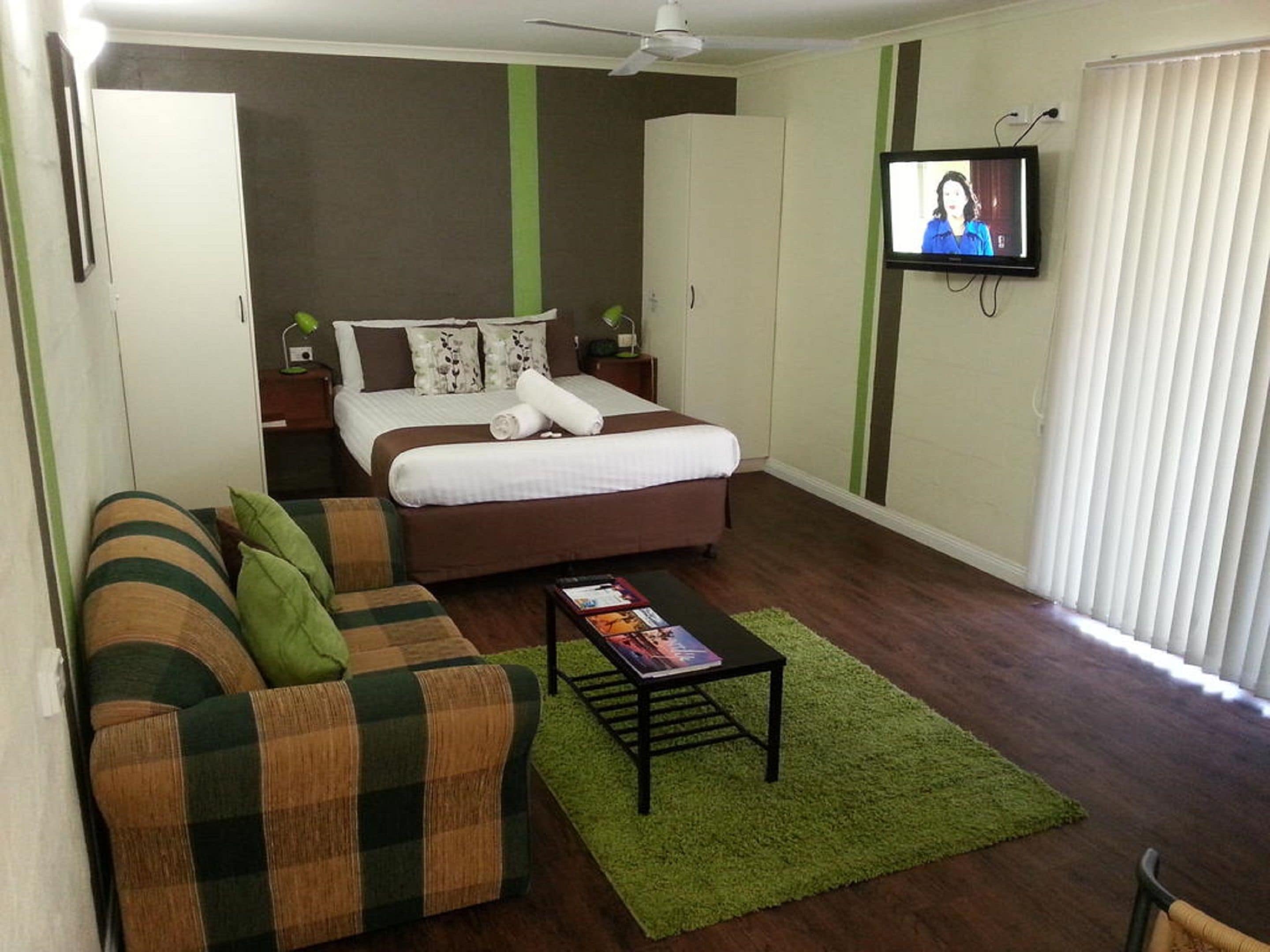 A modern bedroom with a bed, a green sofa, a coffee table, and a TV on the wall.