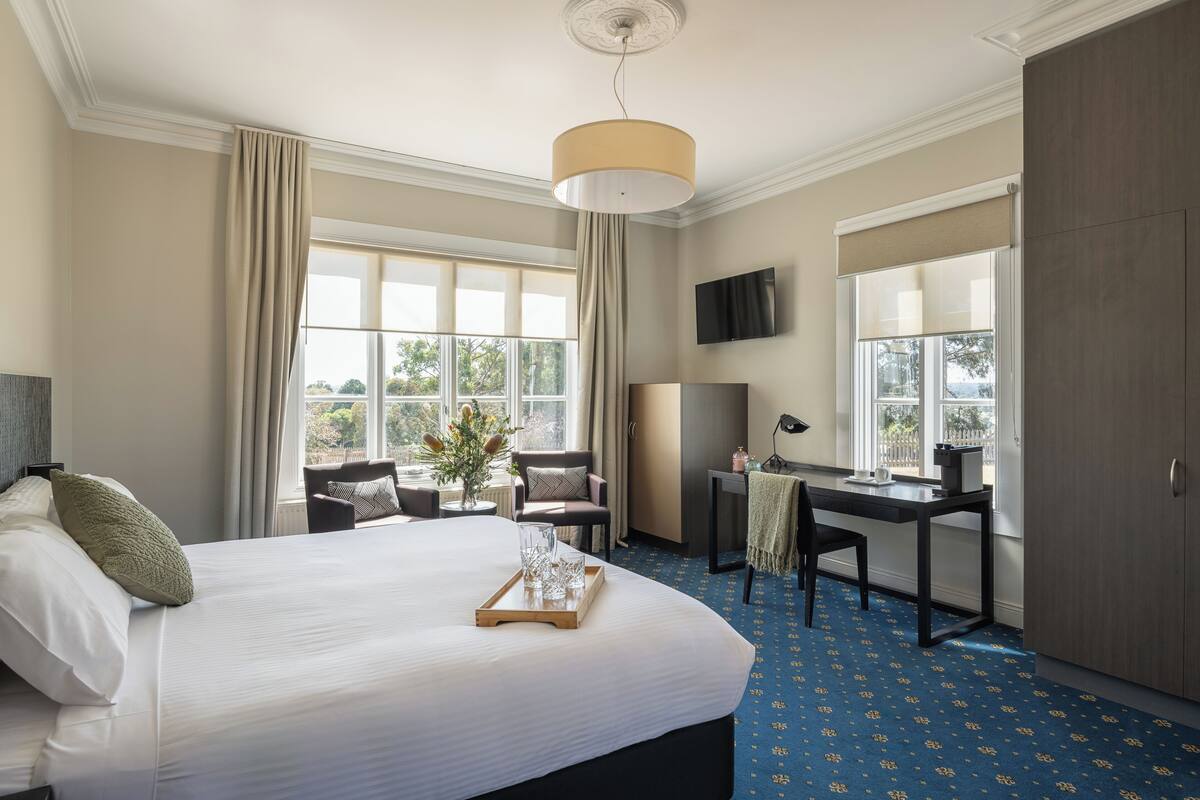 Habitación de hotel con una cama grande, un escritorio, una silla, un televisor y un armario.