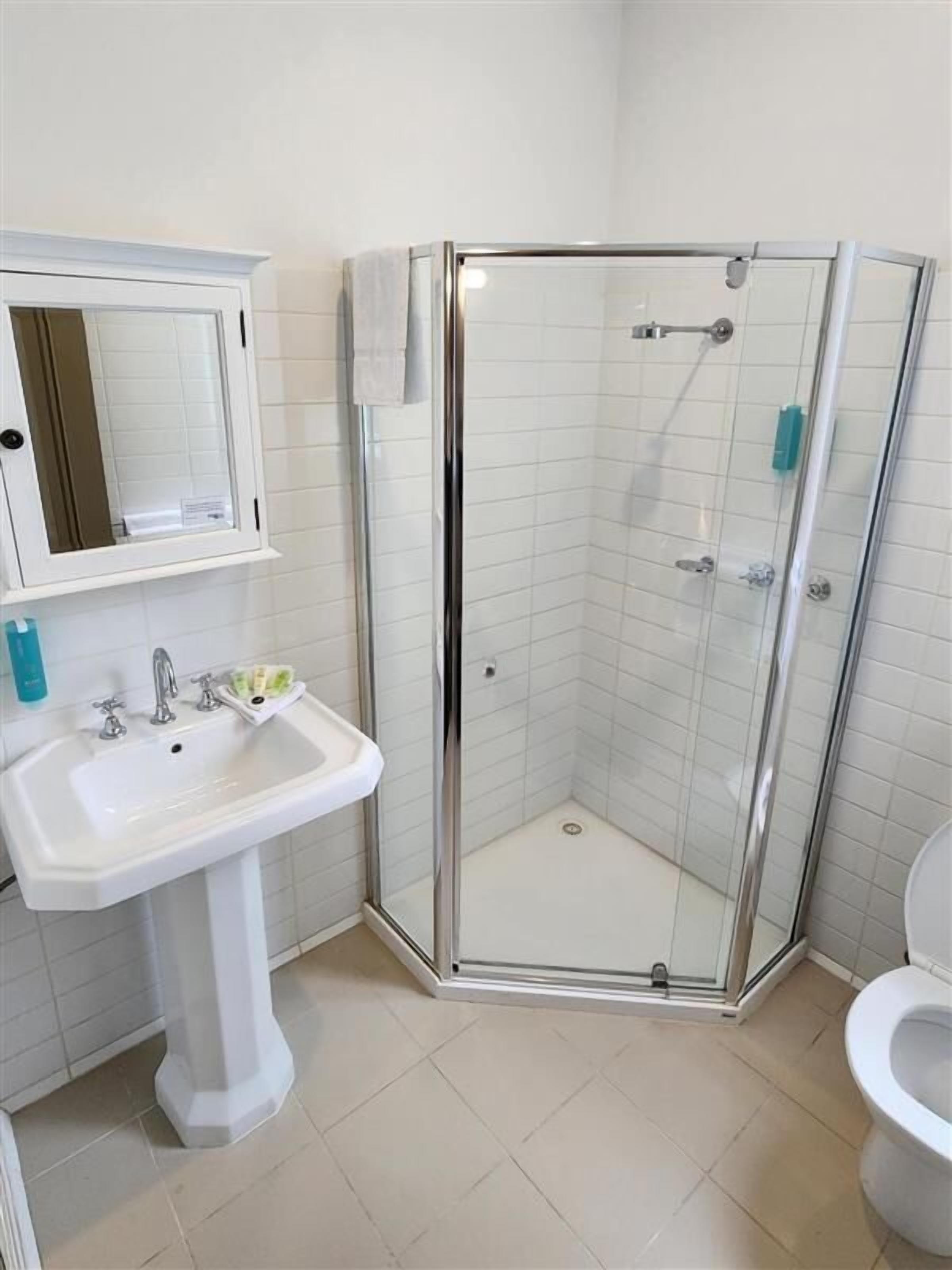 A bathroom with a glass-enclosed shower, a pedestal sink, and a toilet.