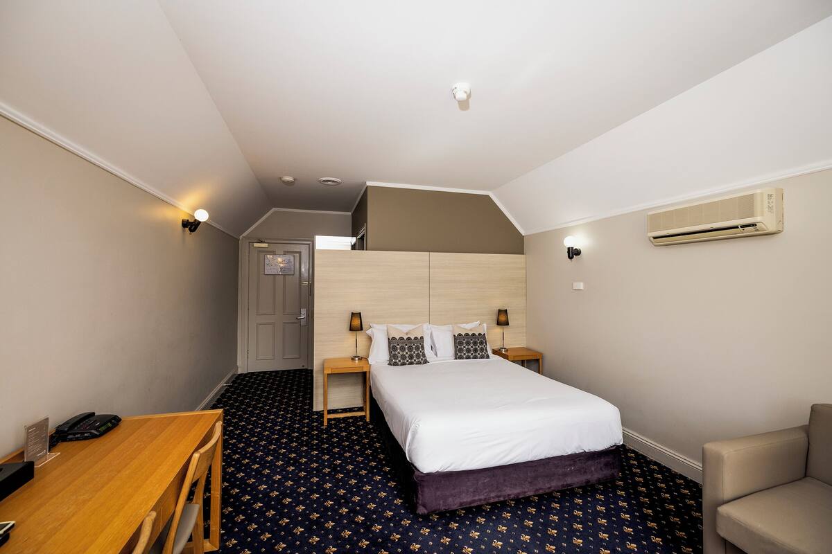 Una habitación de hotel con cama, mesitas de noche, escritorio y una silla.