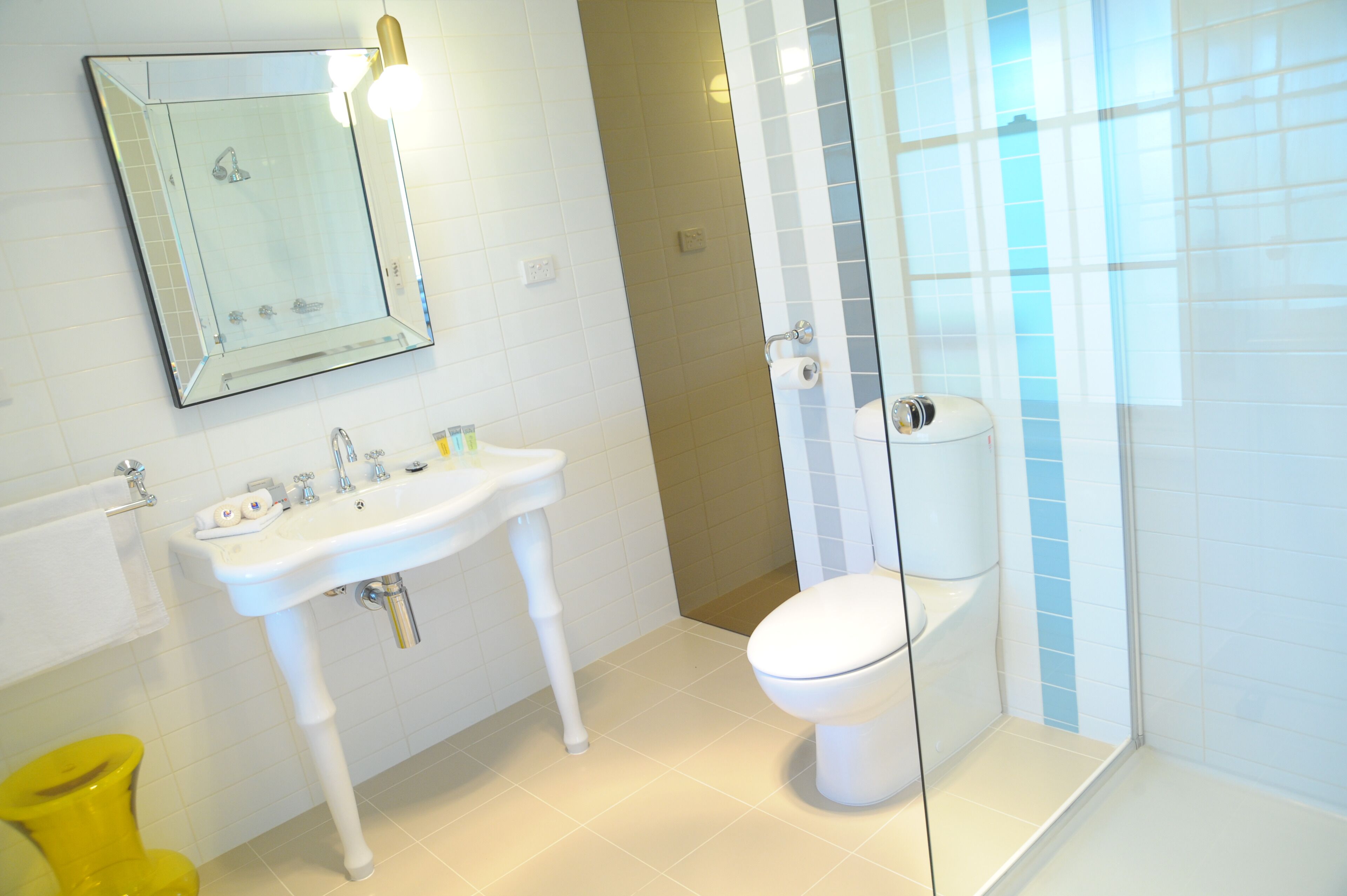 A bathroom with a white sink, mirror, toilet, and yellow trash bin.