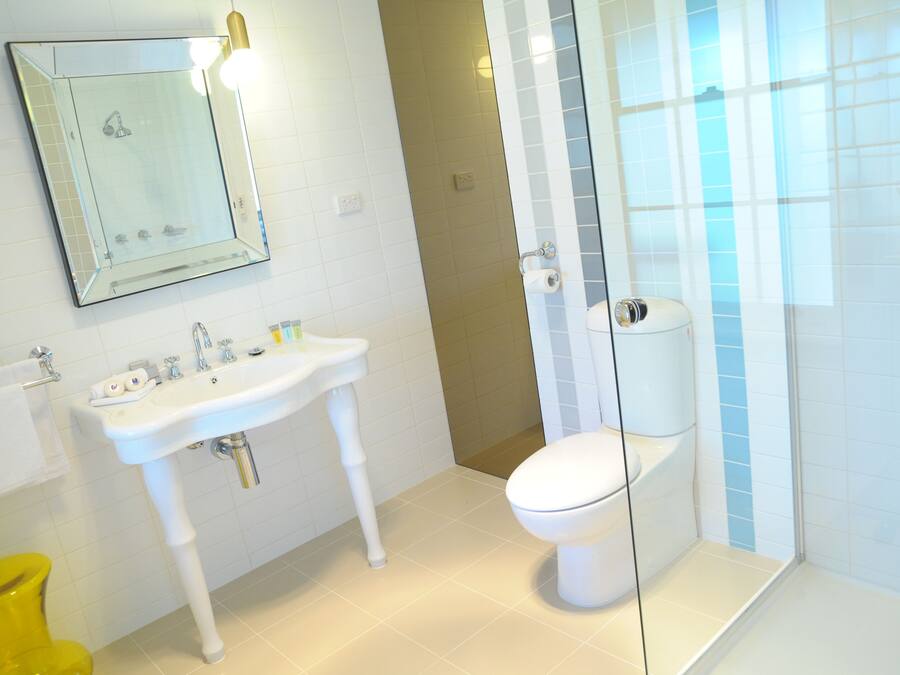A bathroom with a white sink, mirror, toilet, and yellow trash bin.