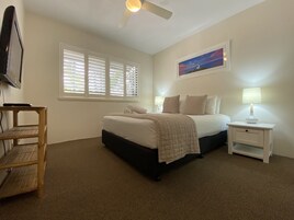 A bedroom with a bed, bedside tables, a lamp, a painting, and a ceiling fan.