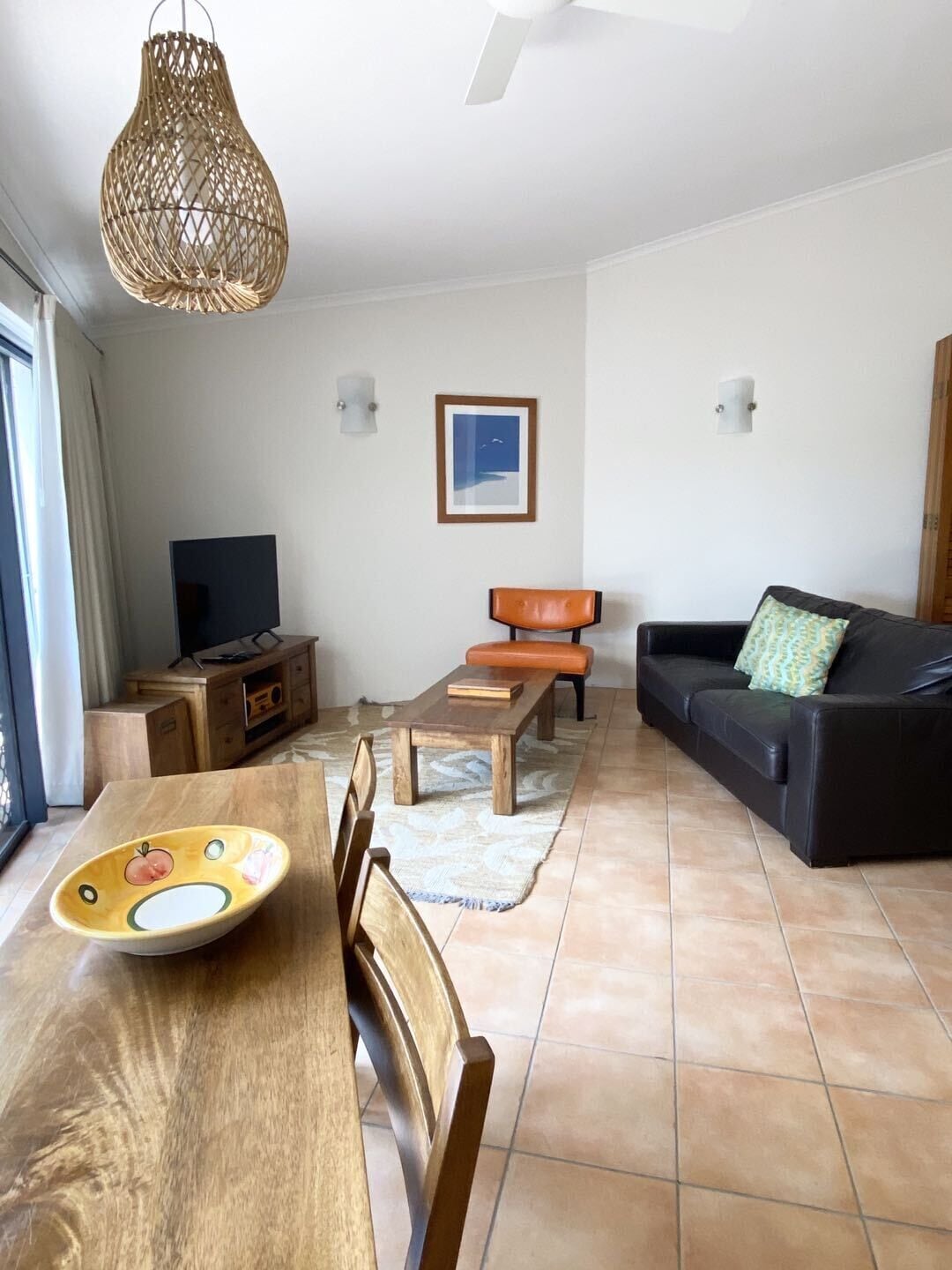 Una sala de estar con una mesa de comedor de madera, un sofá, un televisor y una lámpara colgante.