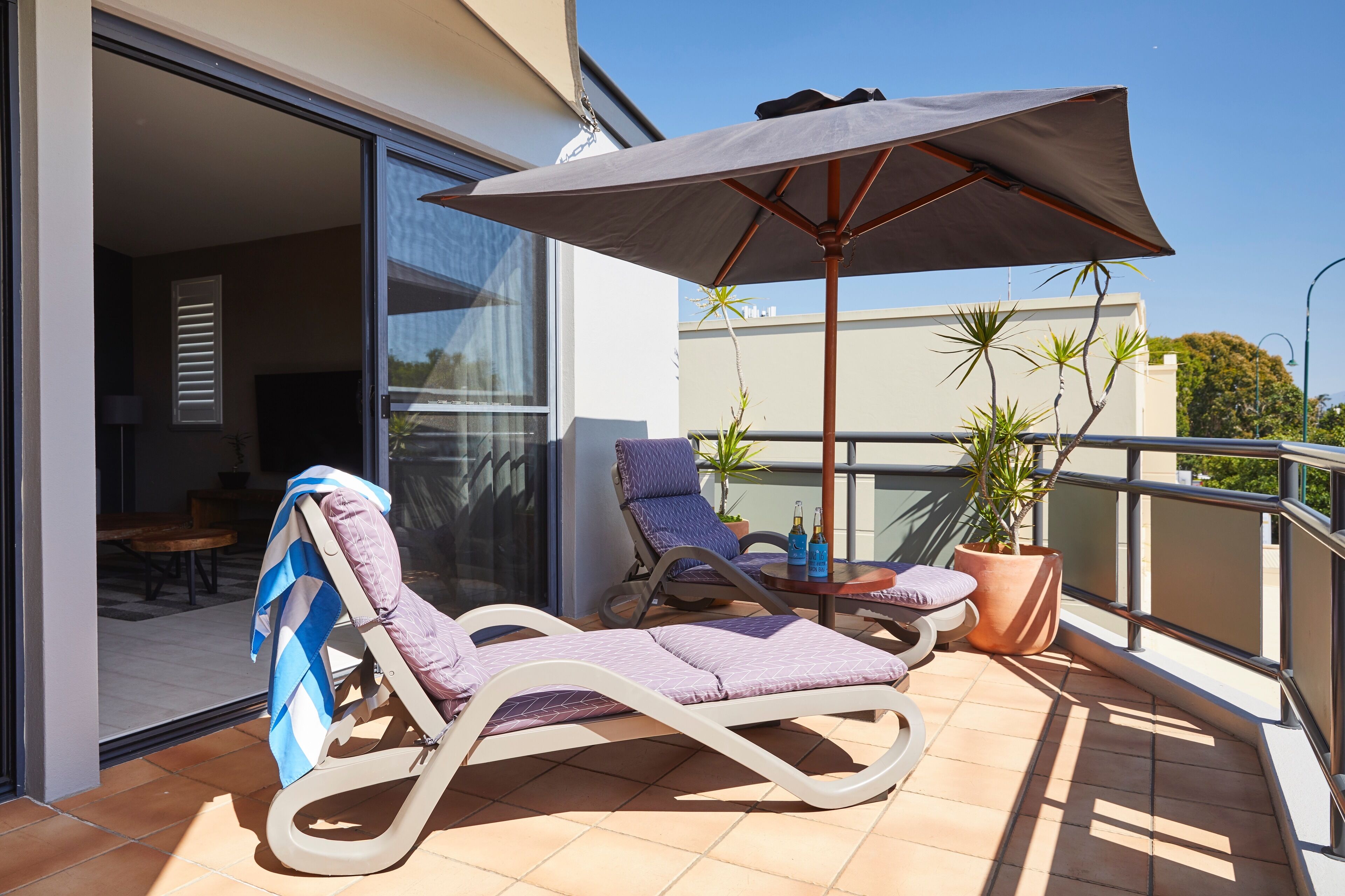 Een balkon met twee loungestoelen, een tafel met flessen en een potplant.
