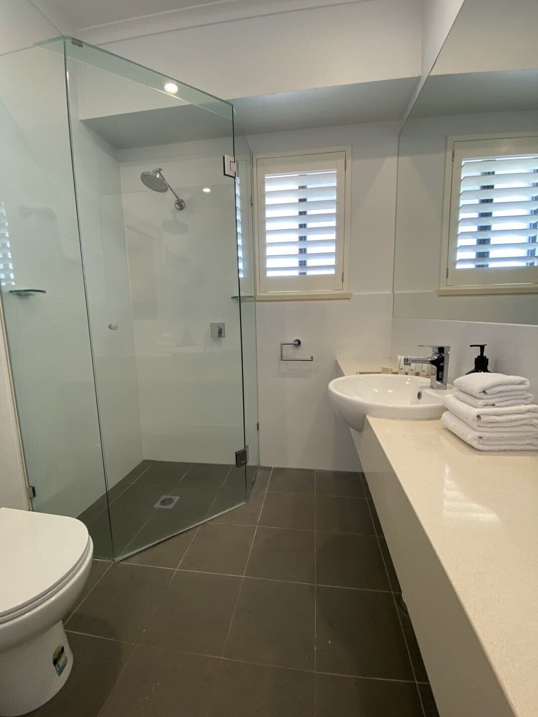 Ein modernes Badezimmer mit einer Duschkabine, Toilette, Waschbecken und einem Fenster mit Jalousien.