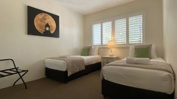 A hotel room with two beds, a ceiling fan, a window with blinds, and a wall-mounted artwork of a moon.