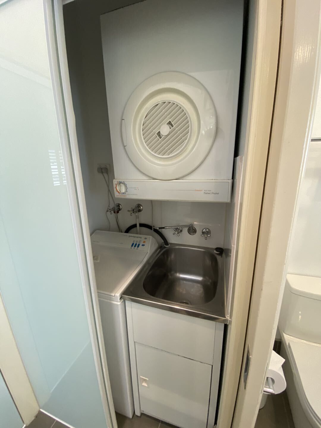 A compact laundry room with a washing machine, a sink, and a toilet.