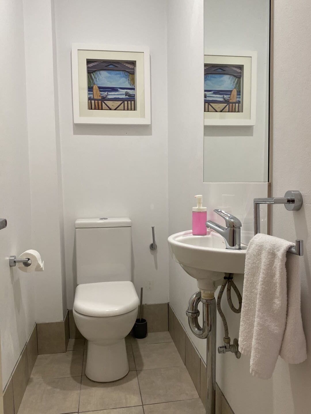 A small bathroom with a toilet, sink, and a framed picture above the toilet.