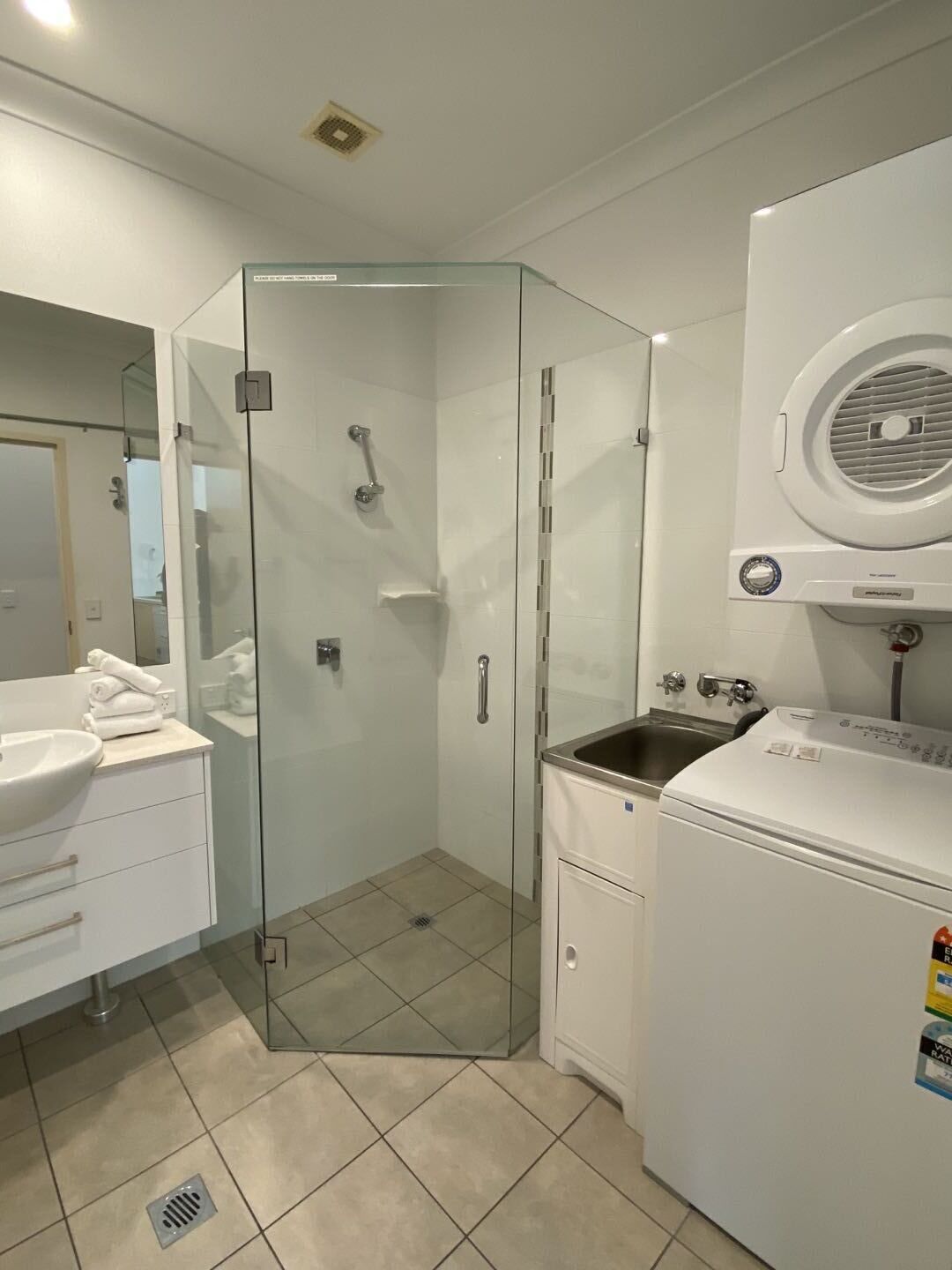Un baño compacto con cabina de ducha de vidrio, lavamanos, inodoro y lavadora integrada.