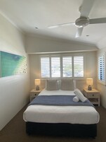 A bedroom with a bed, two bedside tables, a ceiling fan, and a window with blinds.