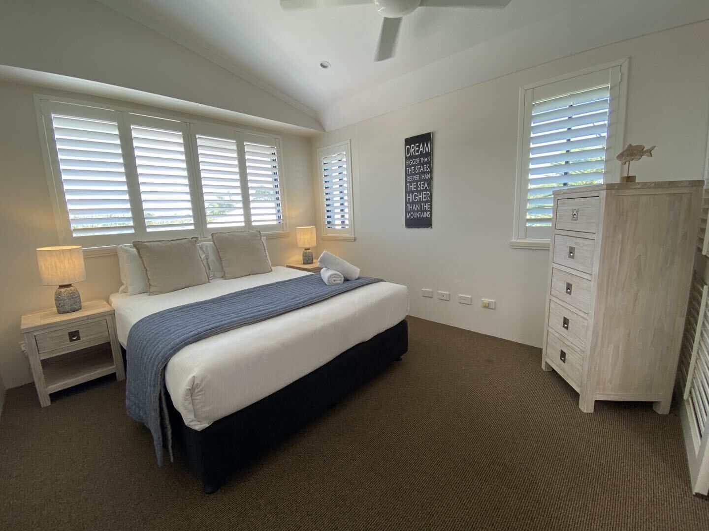 A bedroom with a bed, nightstands, a dresser, and a ceiling fan.