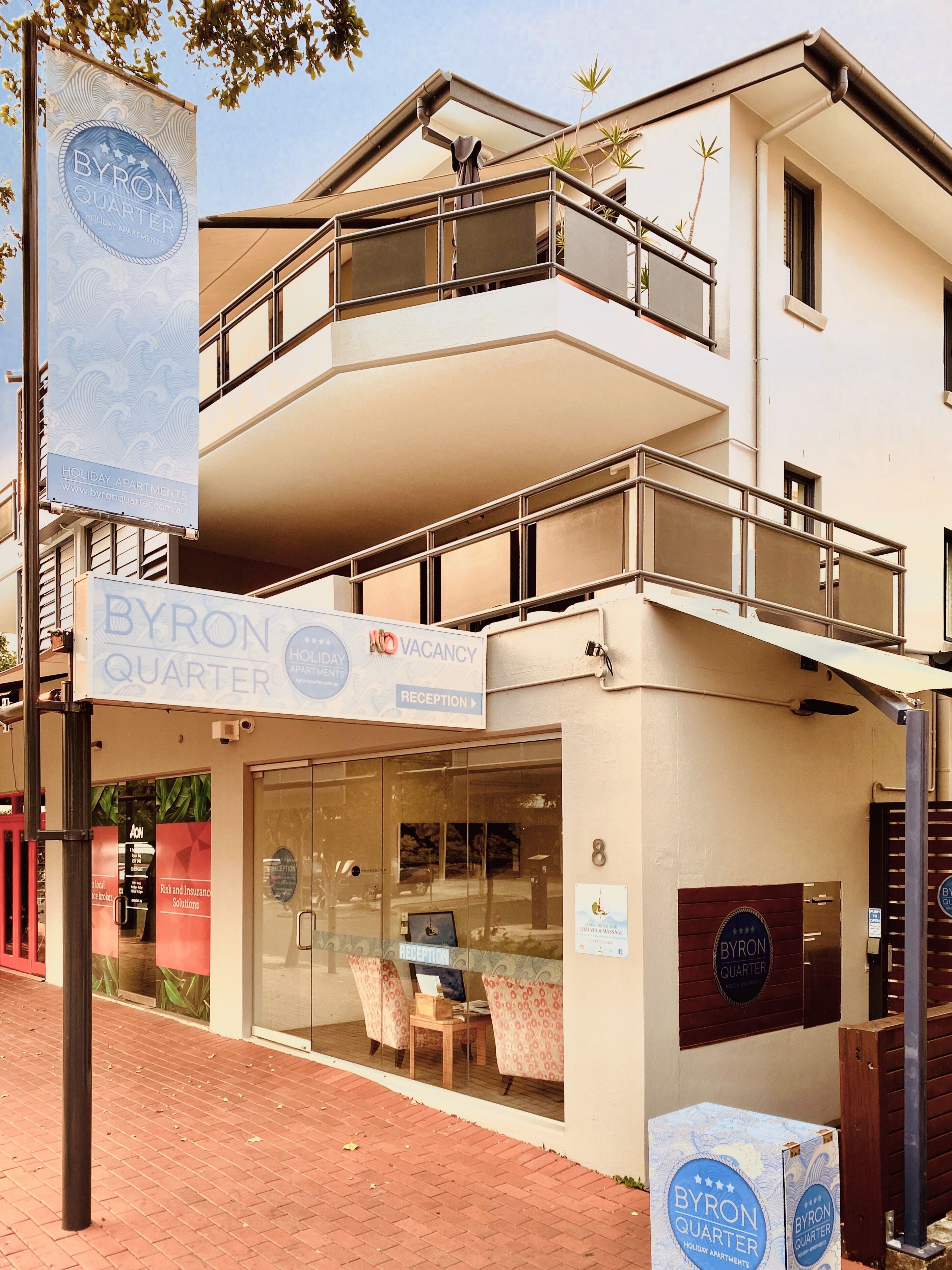 A Byron Quarter holiday apartment building with a reception area, a balcony, and a sign indicating vacancy.