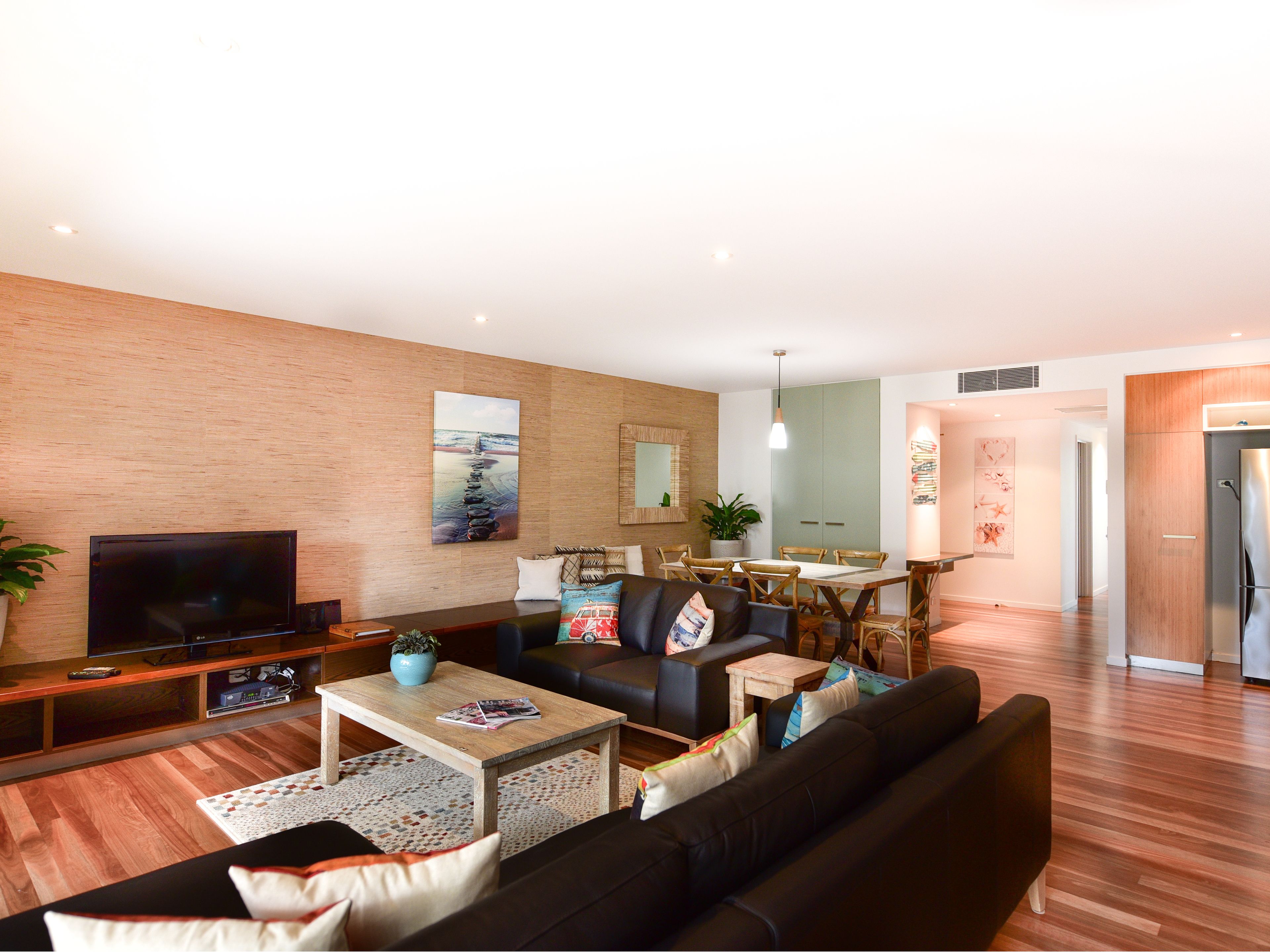 A modern living room with a flat-screen TV, a sofa, a coffee table, and a dining area with a table and chairs.