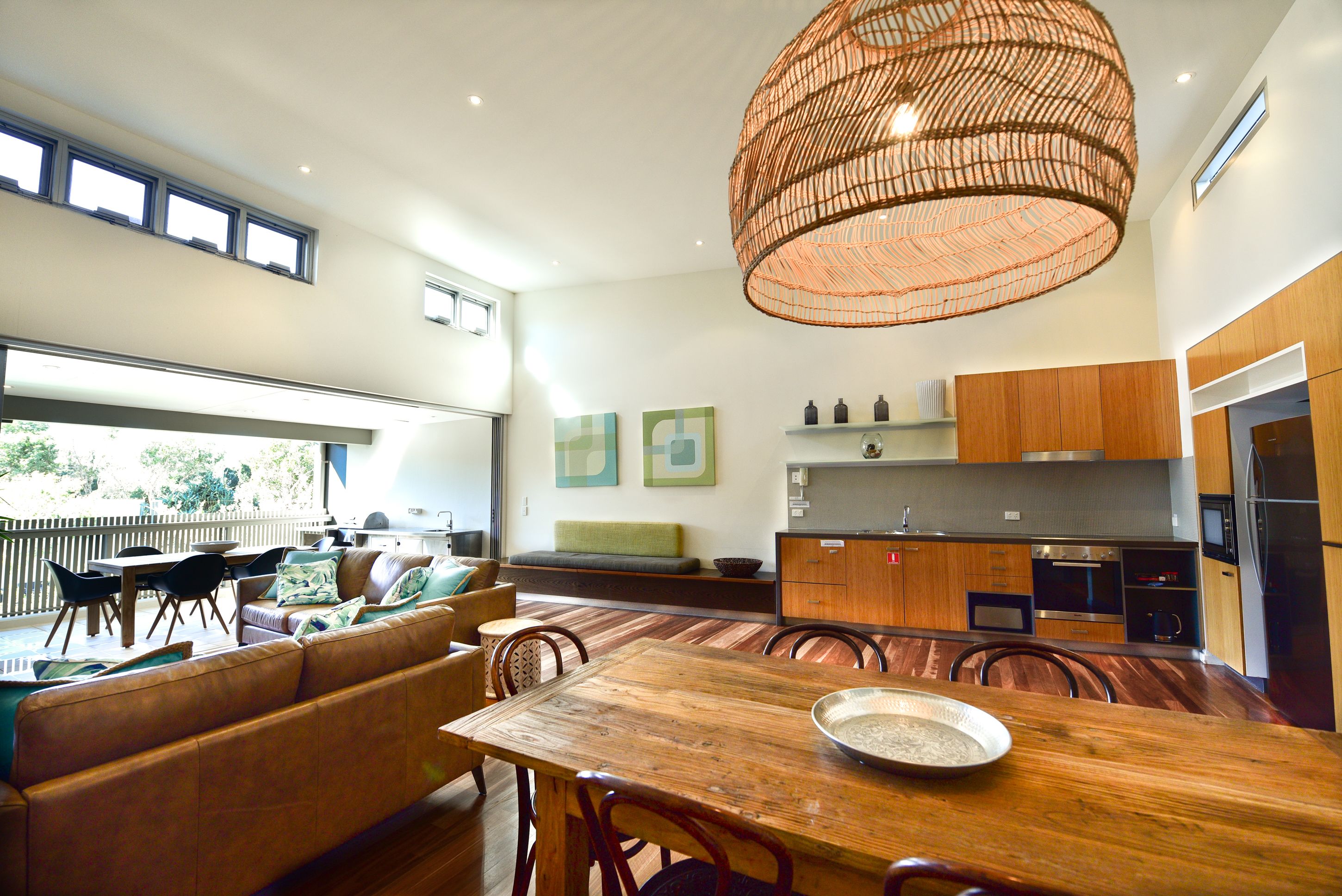 A modern kitchen with wooden cabinets, a dining area with a wooden table, and a large woven ceiling light fixture.