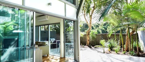 Uma casa moderna com grandes portas de vidro que dão para um pátio com piso de madeira e vista para um jardim exuberante.