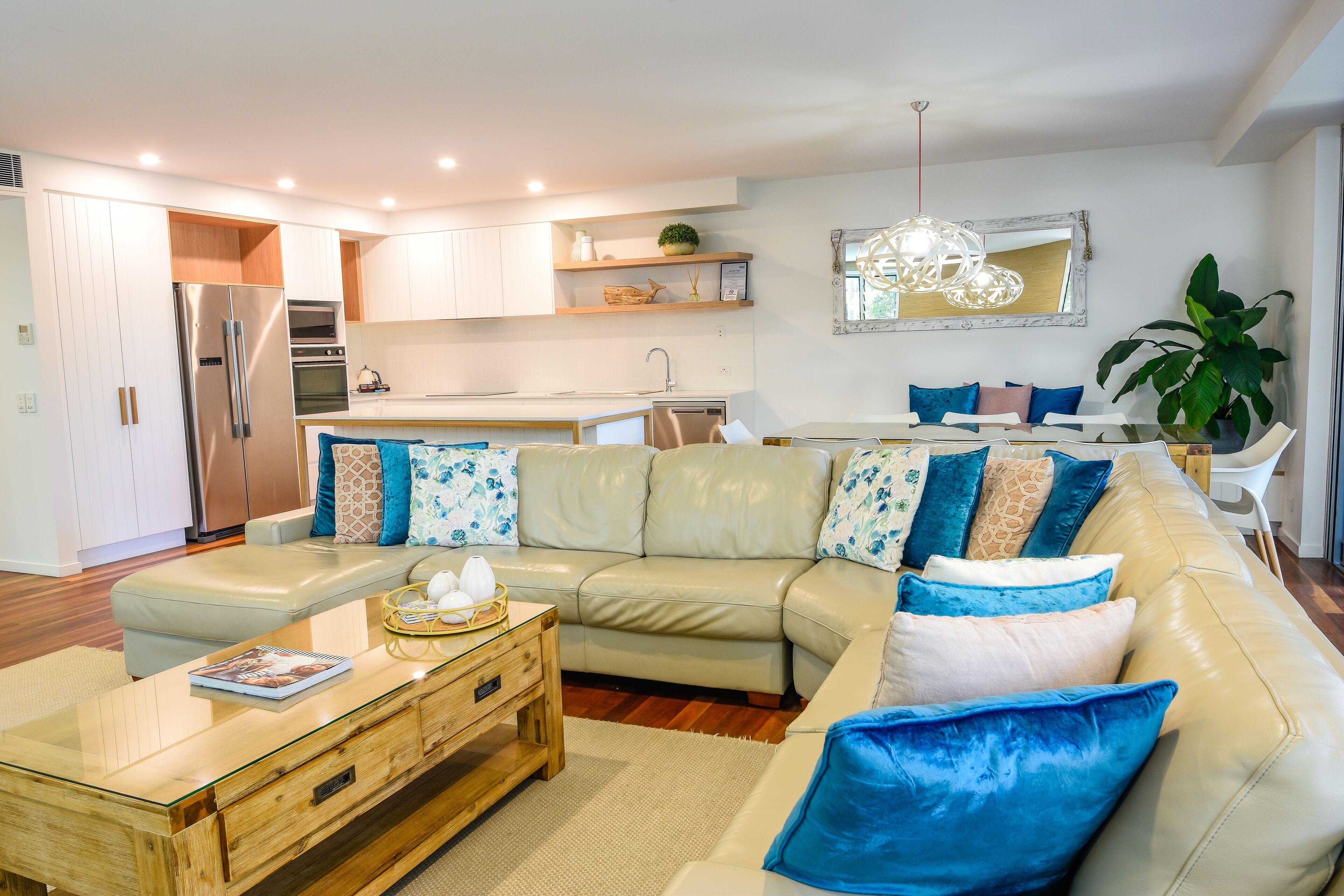 Una sala de estar moderna con un sofá color beige, una mesa de centro de madera y un comedor con una mesa y sillas blancas.