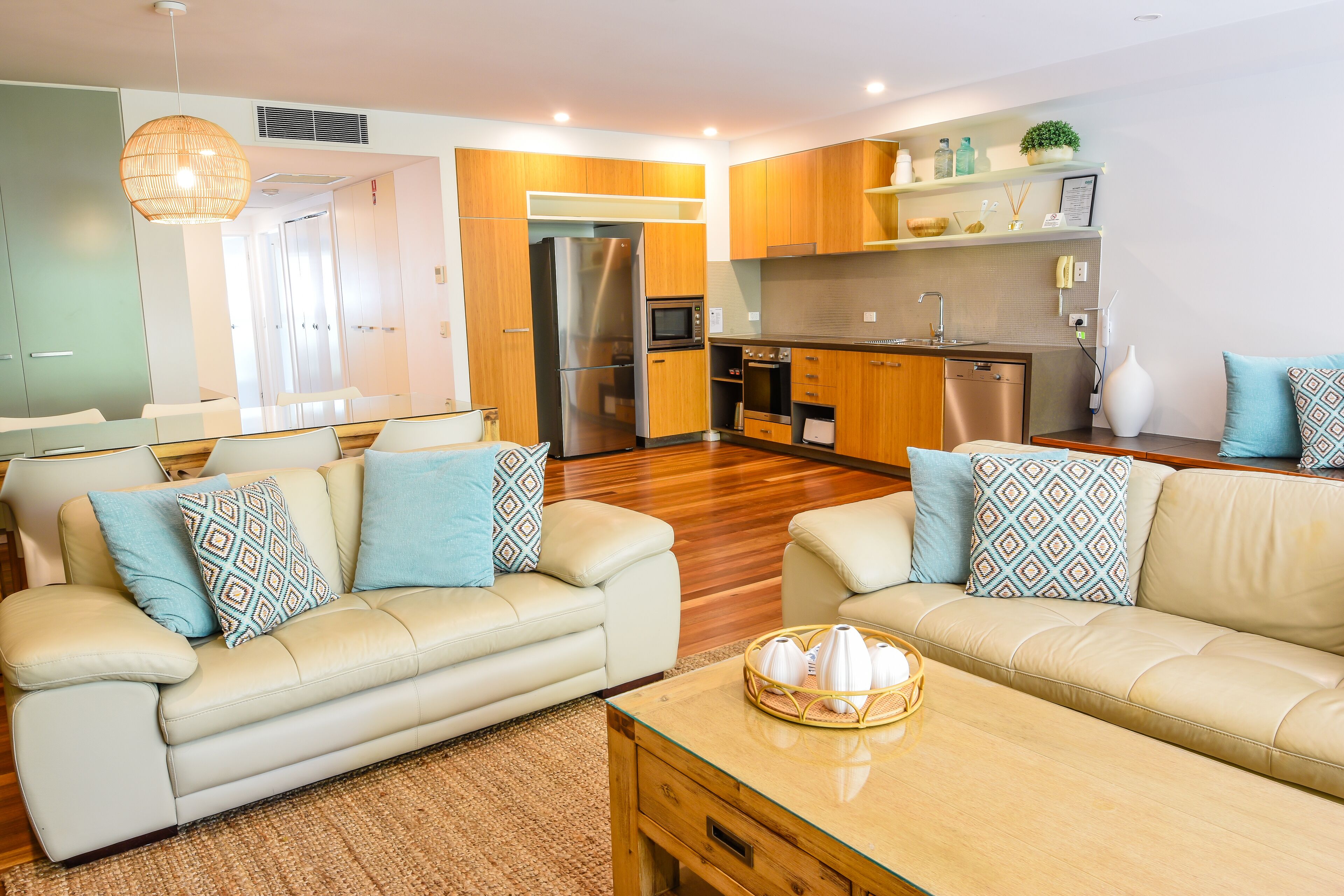 A modern living room with two sofas, a coffee table, and a kitchen area with wooden cabinets and appliances.