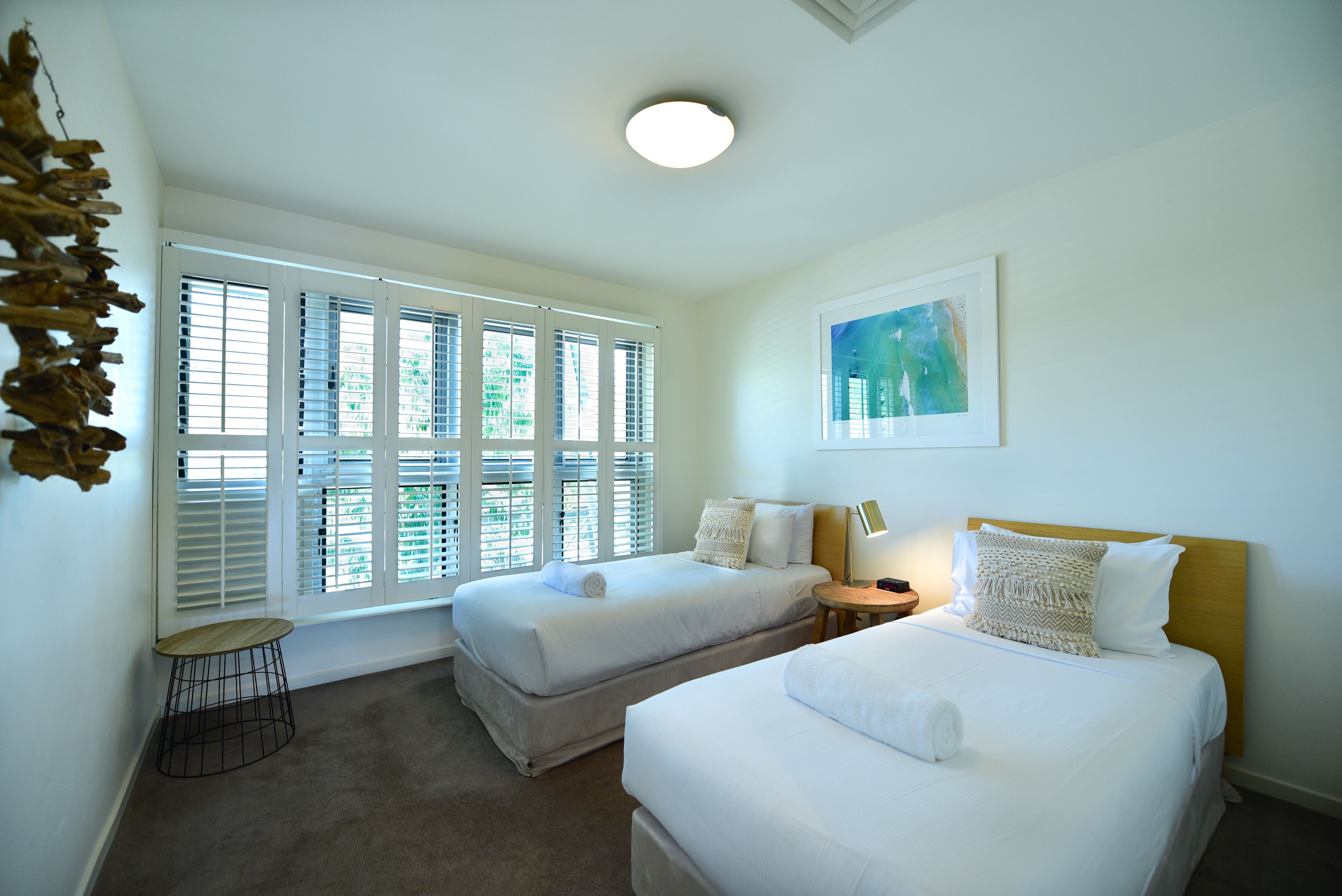 A hotel room with two beds, a small round table, a lamp, and a painting on the wall.