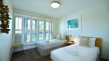 A hotel room with two beds, a small round table, a lamp, and a painting on the wall.