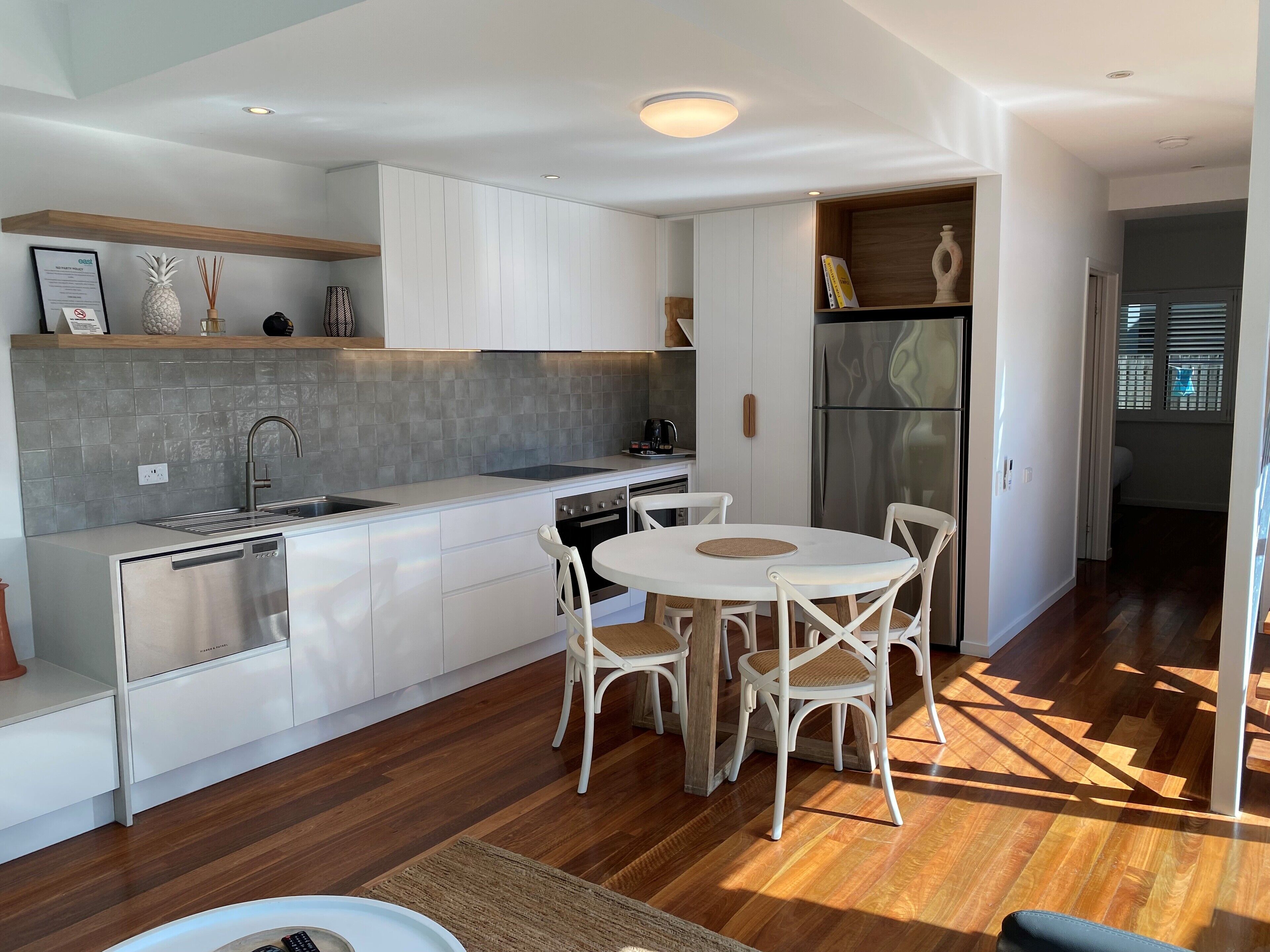 Une cuisine moderne avec des meubles blancs, un réfrigérateur en acier inoxydable et un coin repas avec des chaises blanches.