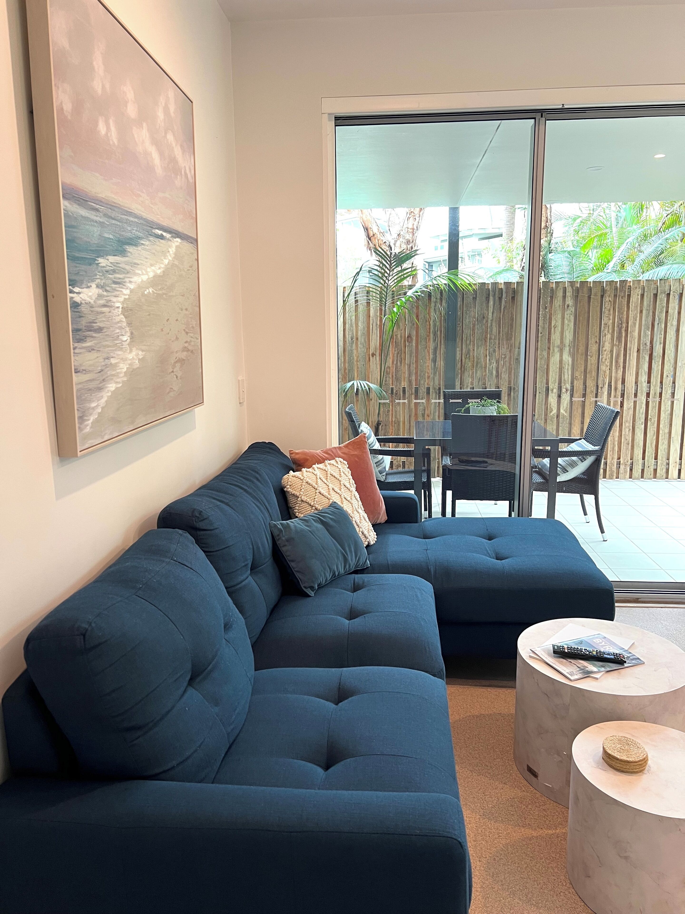 A modern living room with a dark blue sectional sofa, a coffee table, and a large window overlooking a wooden deck.