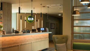 A reception desk with a B&B Hotels sign, a green armchair, and a modern interior design. - B&B HOTEL Ipswich (Ipswich)