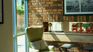 A room with a brick wall, a large window, a green armchair, a table, and a lamp. - B&B HOTEL Ipswich (Ipswich)
