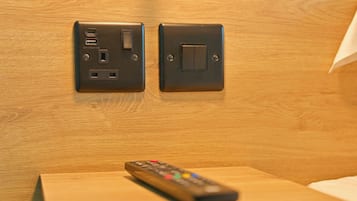 Un control remoto sobre una mesa de madera con un enchufe e interruptor fijados a la pared.