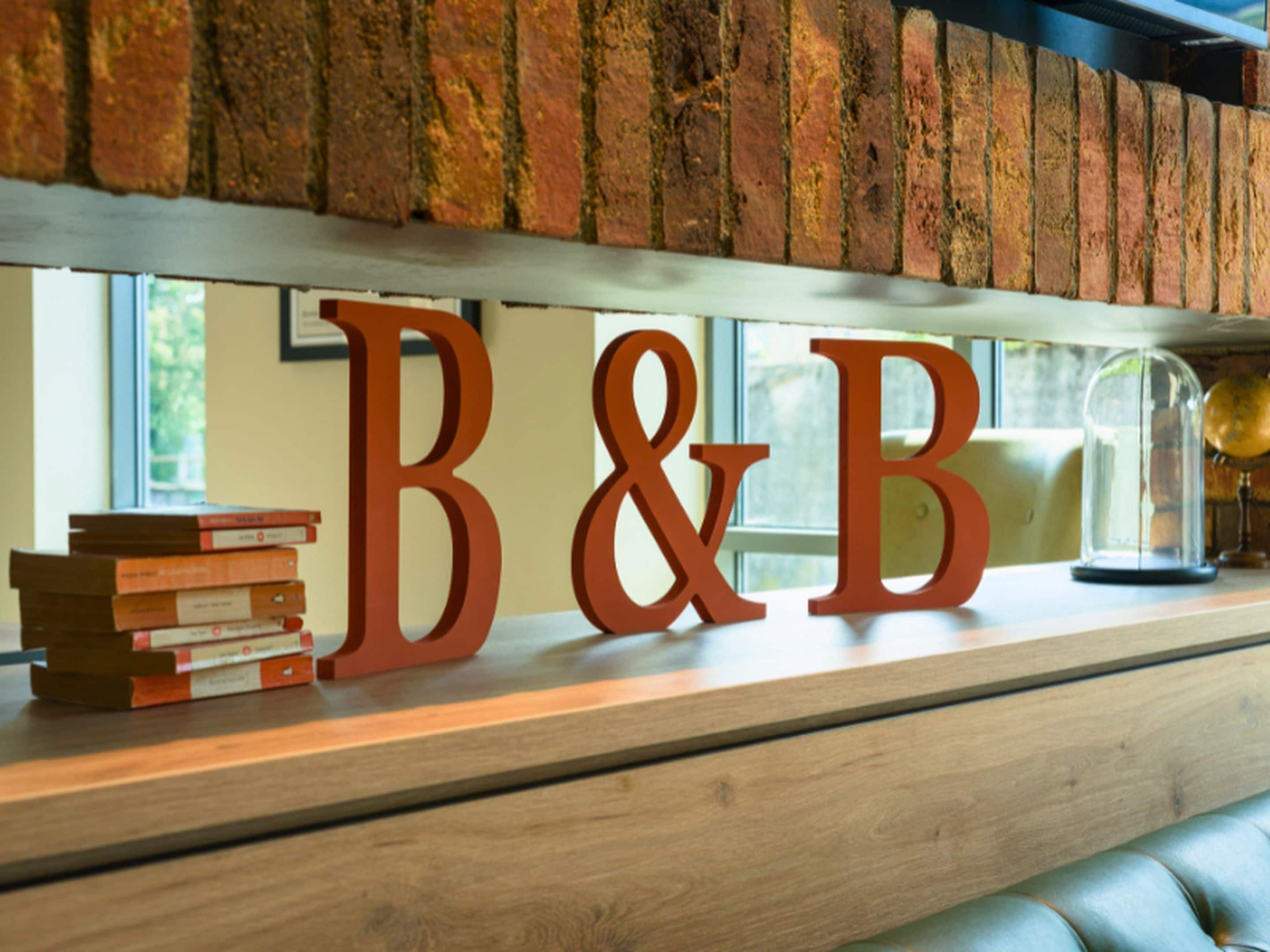 A wooden shelf with large wooden letters spelling "B&B" above a stack of books.