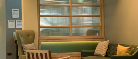 A modern lounge area with a green sofa, a wooden chair, and a small table.