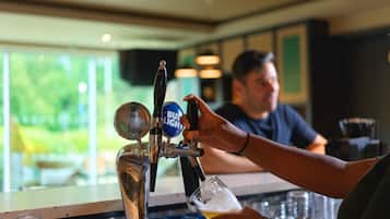 A bar tap with multiple beer options, a person pouring beer into a glass, and a bar counter with glasses.
