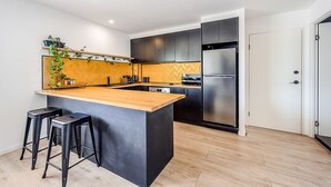 A modern kitchen with a central island, black cabinets, and stainless steel appliances. - The Lord Byron (Byron Bay)