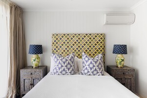 Una habitación de hotel con cama, dos mesitas de noche, un cabecero estampado y un equipo de aire acondicionado.