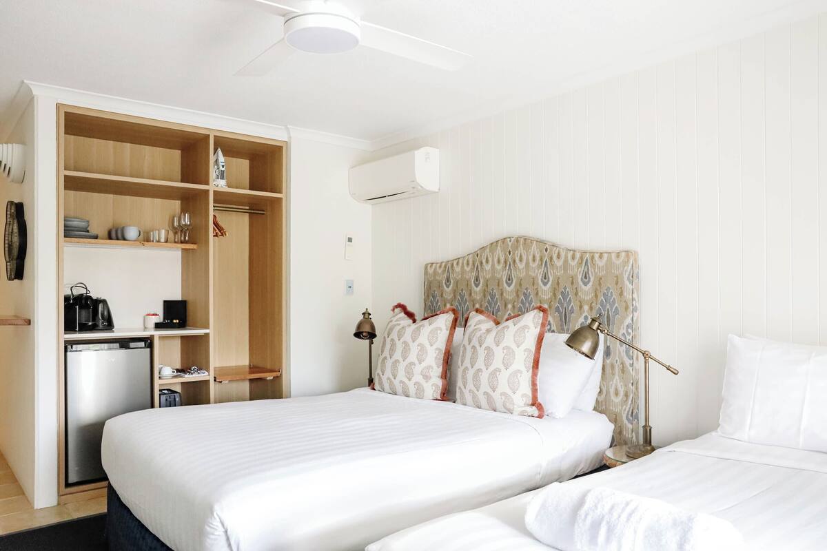 Ein Hotelzimmer mit einem großen Bett, einem Kleiderschrank, einem Schreibtisch mit Kaffeemaschine und einer Klimaanlage.