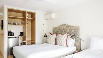 A hotel room with a large bed, a wardrobe, a desk with a coffee maker, and an air conditioning unit.