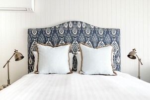 Una cama con cabecera estampada, dos lámparas de noche y una colcha blanca.