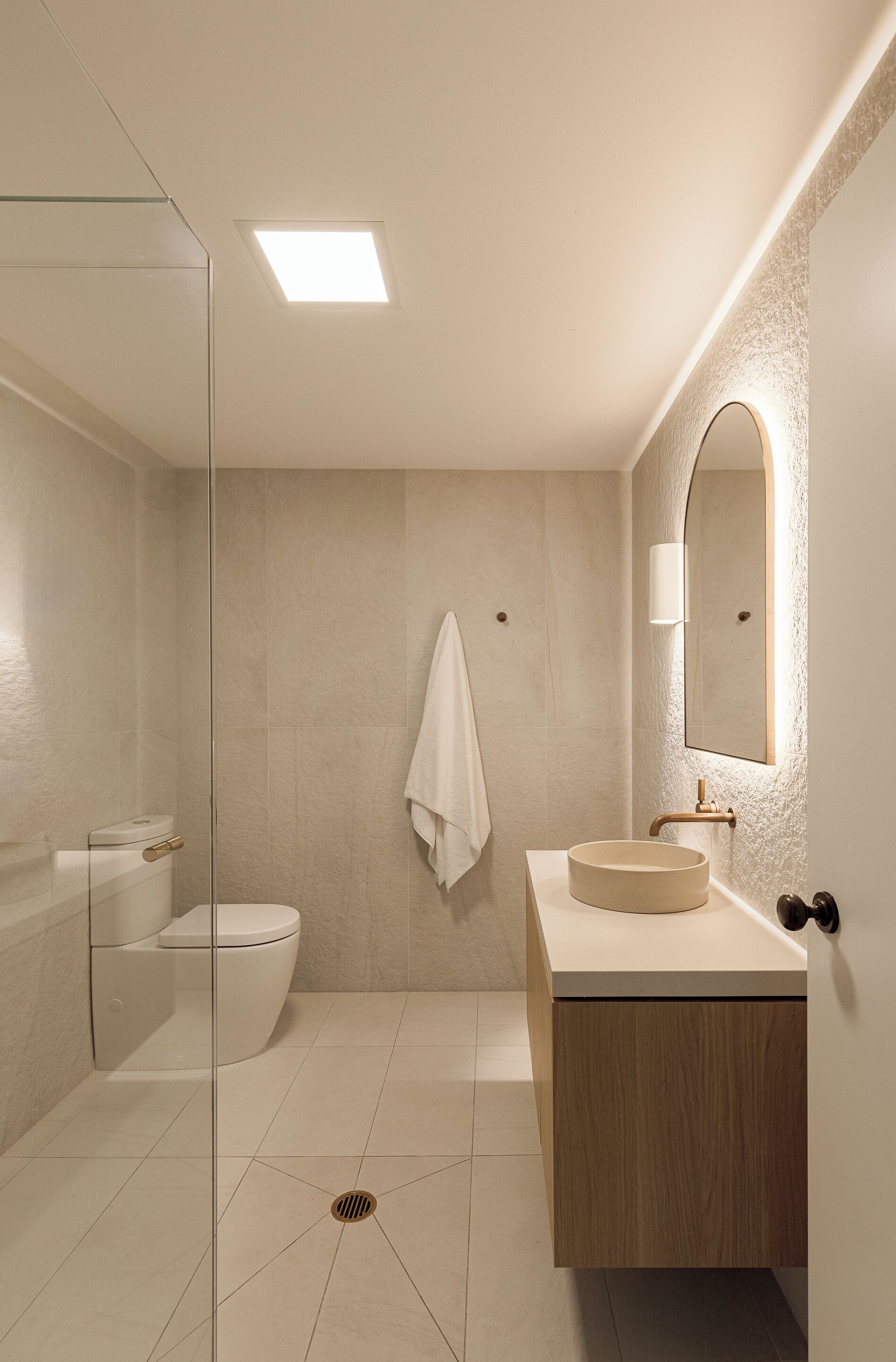 A modern bathroom with a glass shower enclosure, a toilet, a sink with a wooden cabinet, and a mirror with a textured wall.
