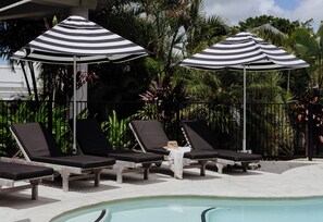 A poolside area with striped umbrellas, lounge chairs, and tropical plants.