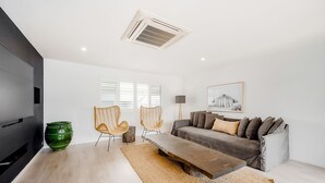 A modern living room with a flat-screen TV, a sofa, two chairs, a coffee table, and a large window. - The Lord Byron (Byron Bay)